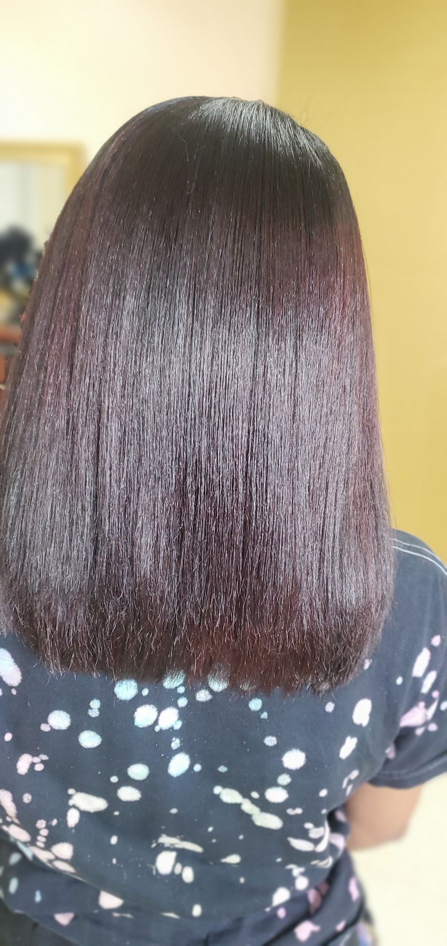Back view of straight, shoulder-length dark hair with reddish highlights over a black polka-dot shirt