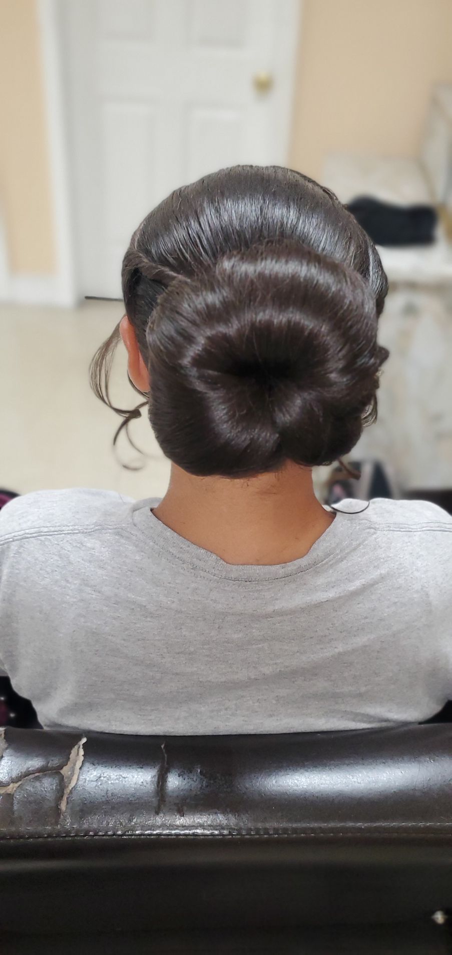 Back view of an elegant dark hair bun hairstyle on a person seated indoors.