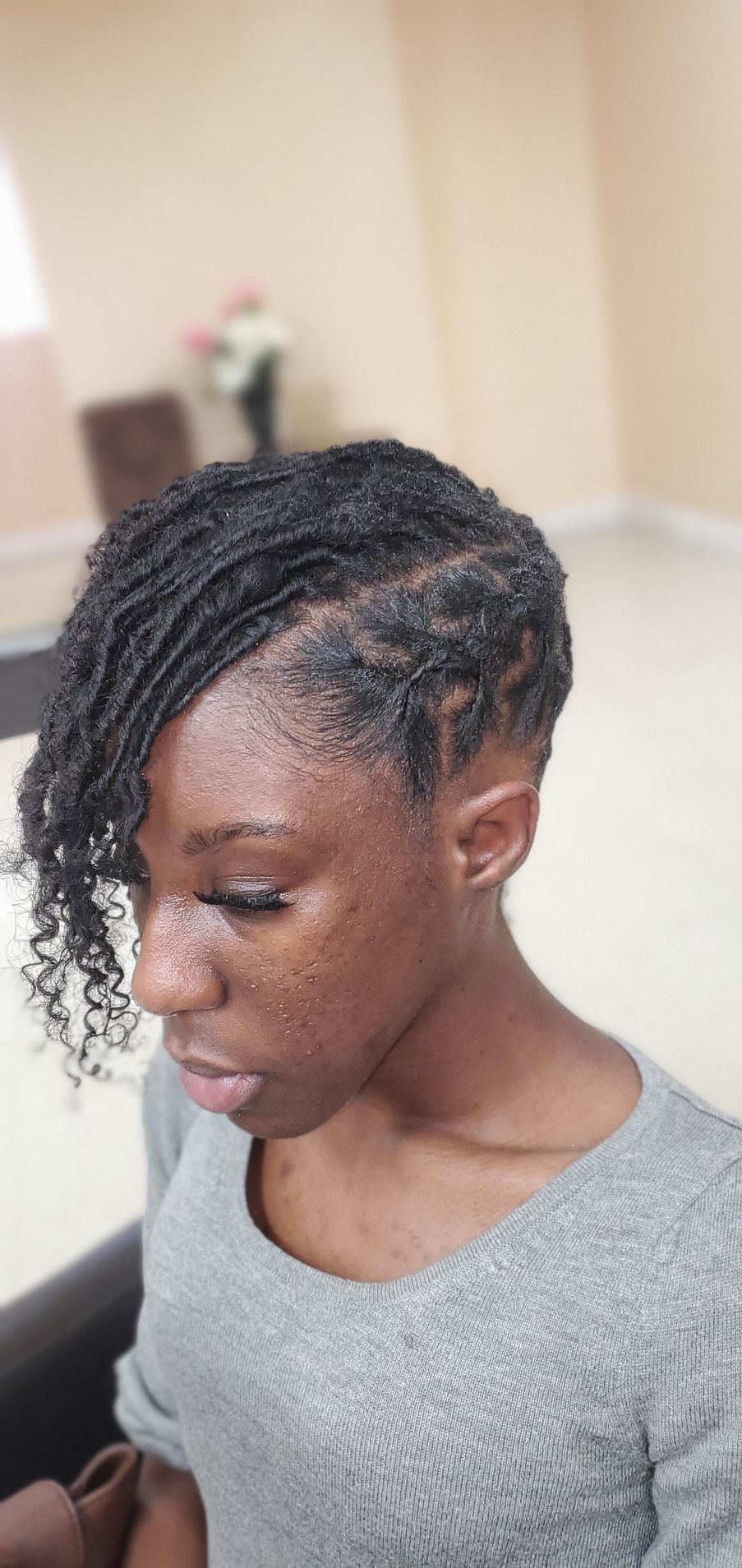 Woman with braided hair looking down in a gray sweater indoors