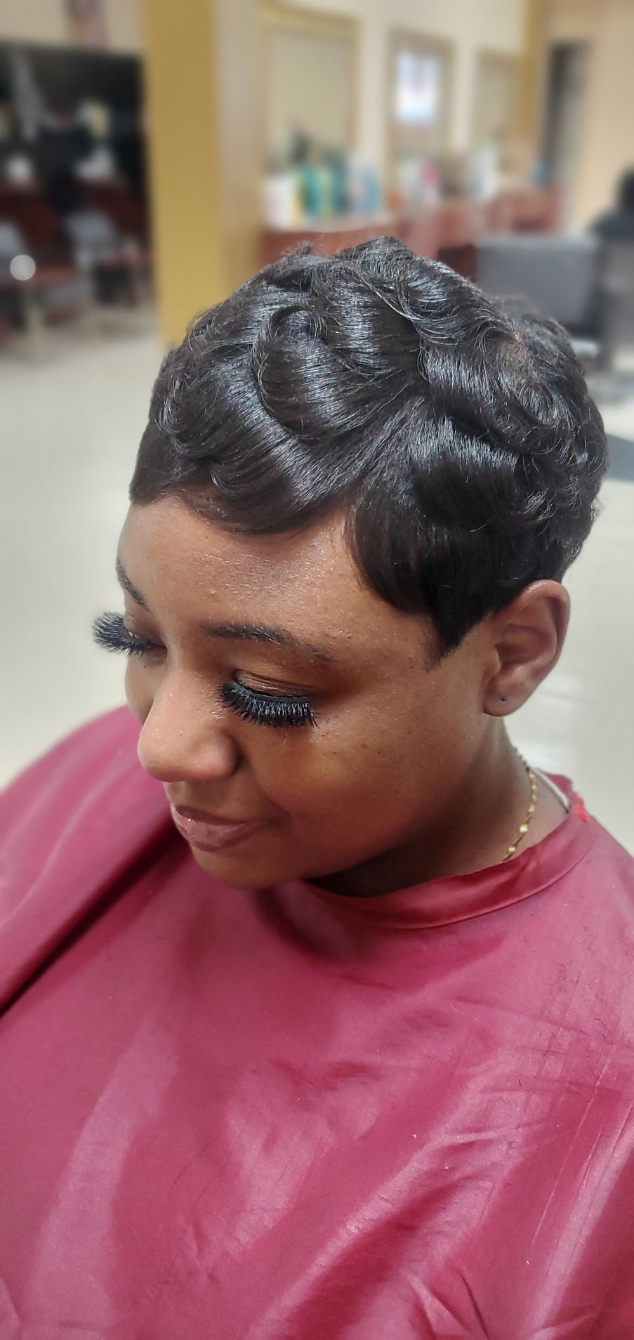 Short textured haircut with styled edges, wearing a pink cape in a salon chair