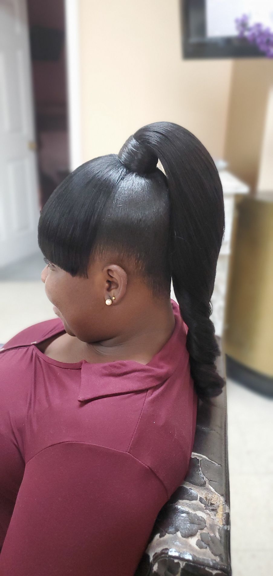 Woman with sleek black ponytail seated in a salon chair, wearing a maroon top.