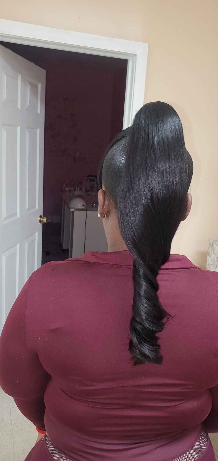 Person with long braided ponytail wearing a maroon top, viewed from behind in a doorway.