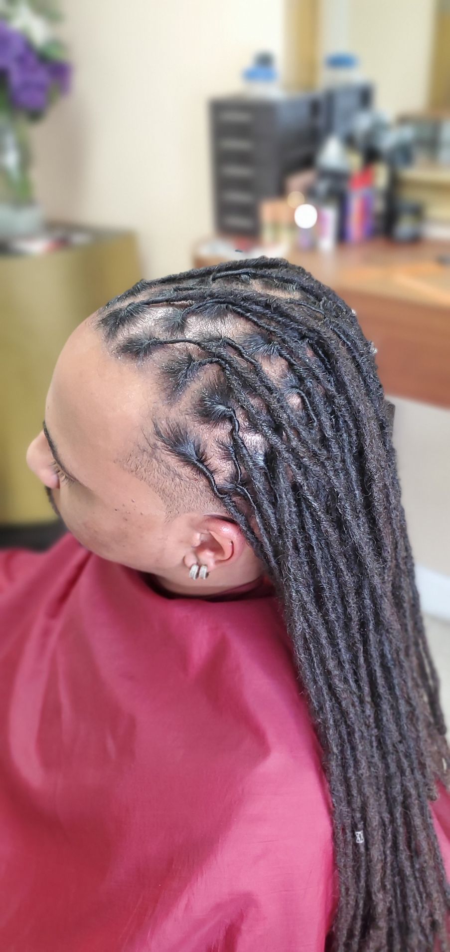 Close-up of braided hairstyle on a person seated in a salon chair, with shaved sides and long braids falling back