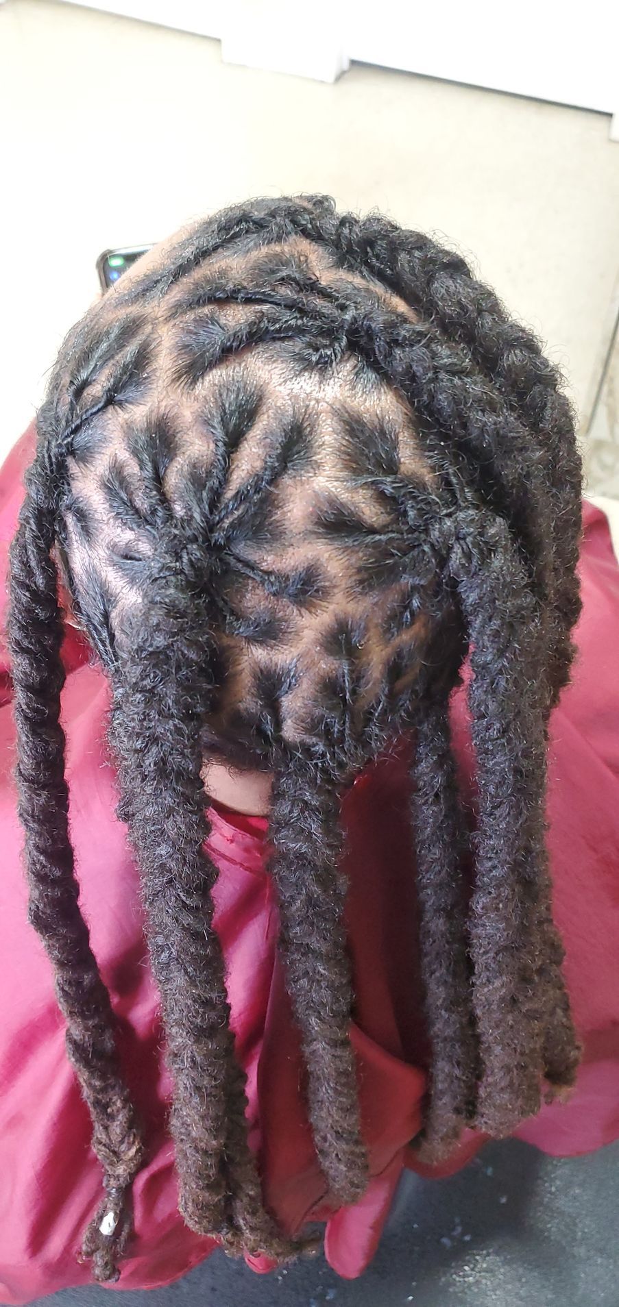 Person with long braided hair leaning forward in a burgundy top against a light wall.
