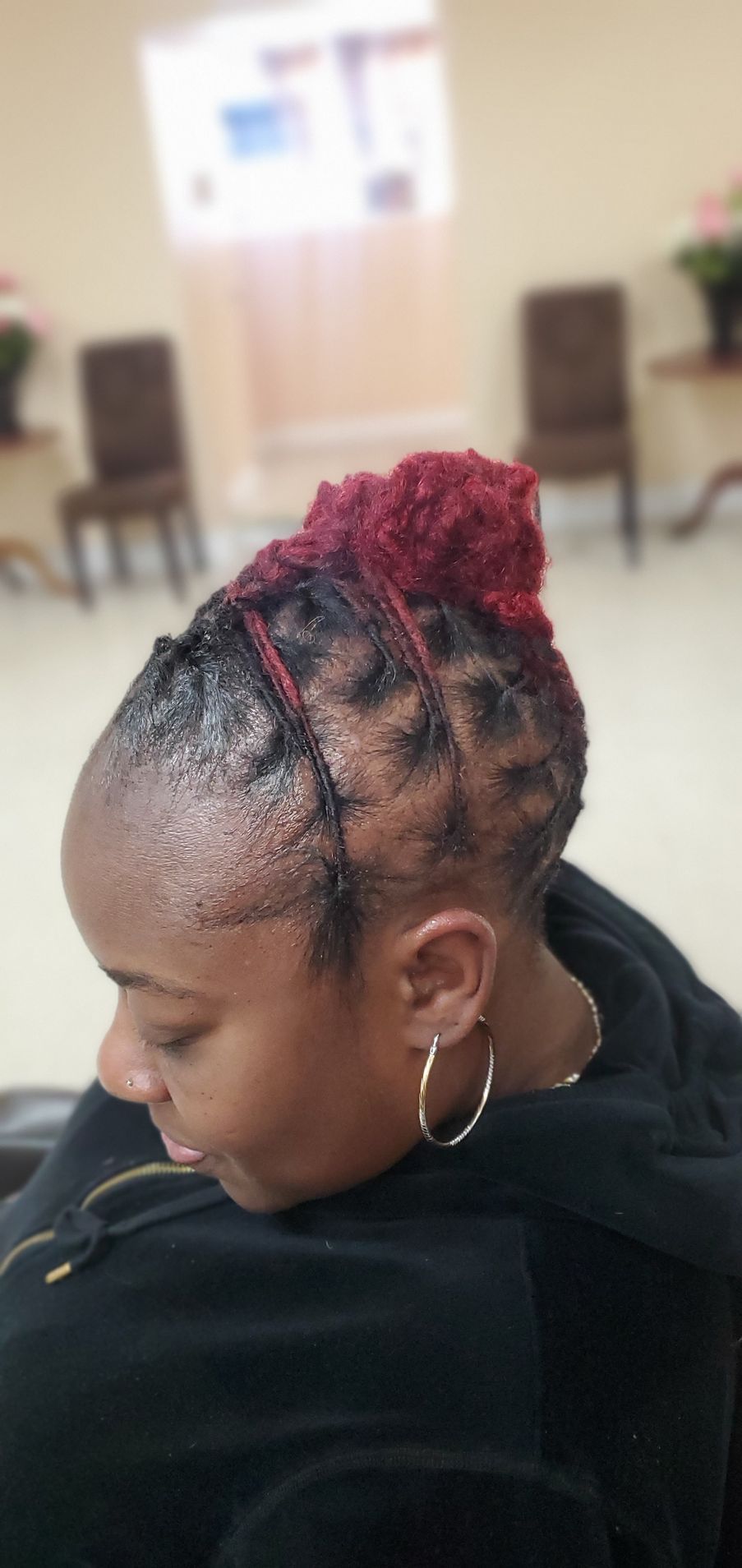 Person with red braided hair and hoop earrings, looking down in a blurred indoor setting.