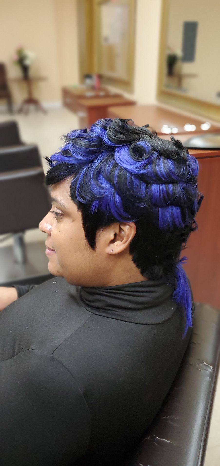 Person with bright blue hair sitting in a salon chair, side profile.