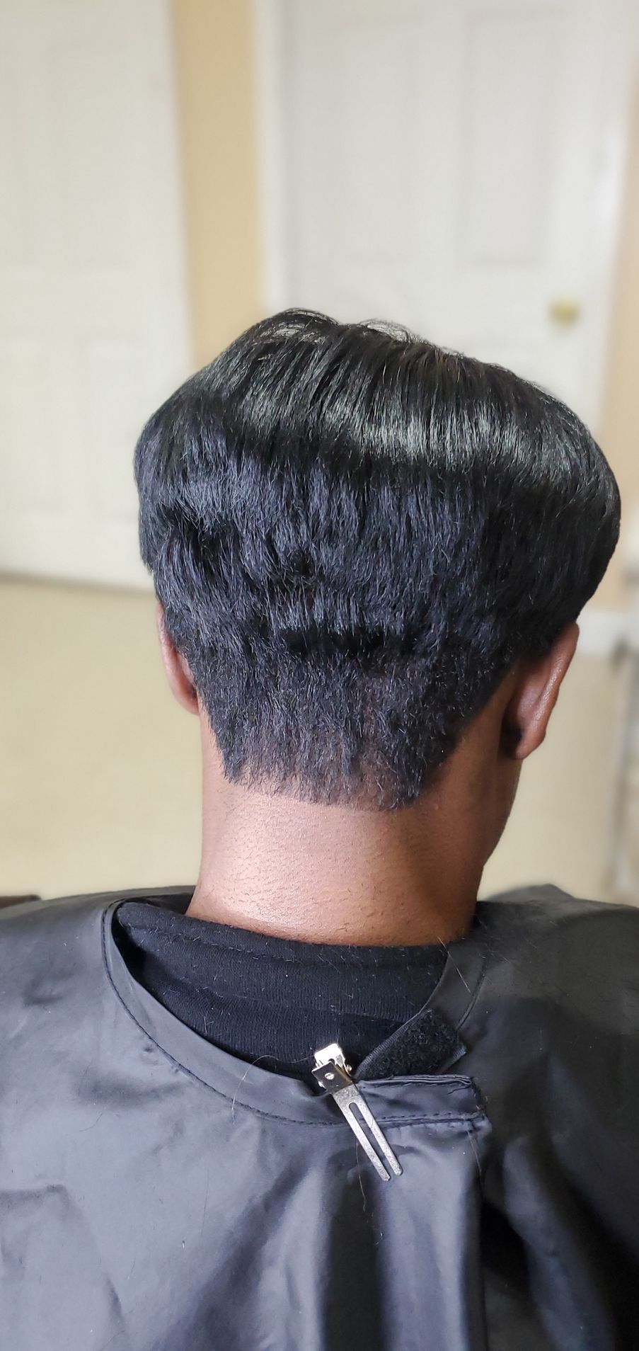 Back view of a person with a black haircut cape, showing a short tapered haircut at a salon