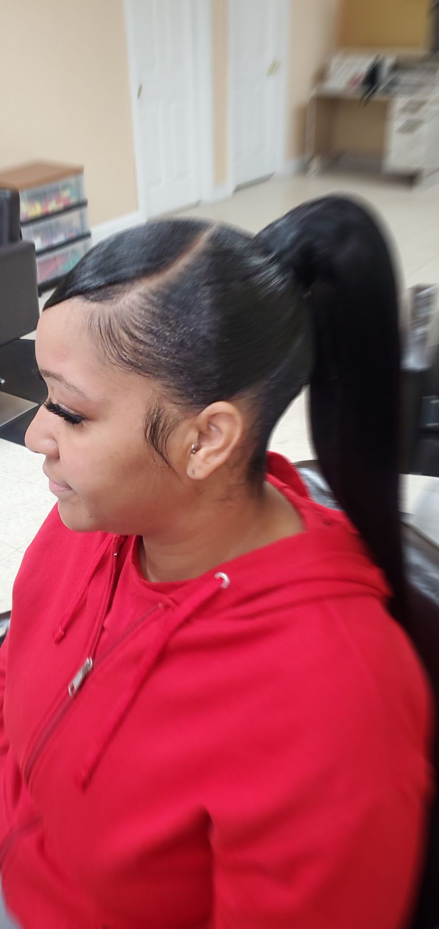 Person in a red hoodie with hair in a ponytail, sitting indoors in side profile.