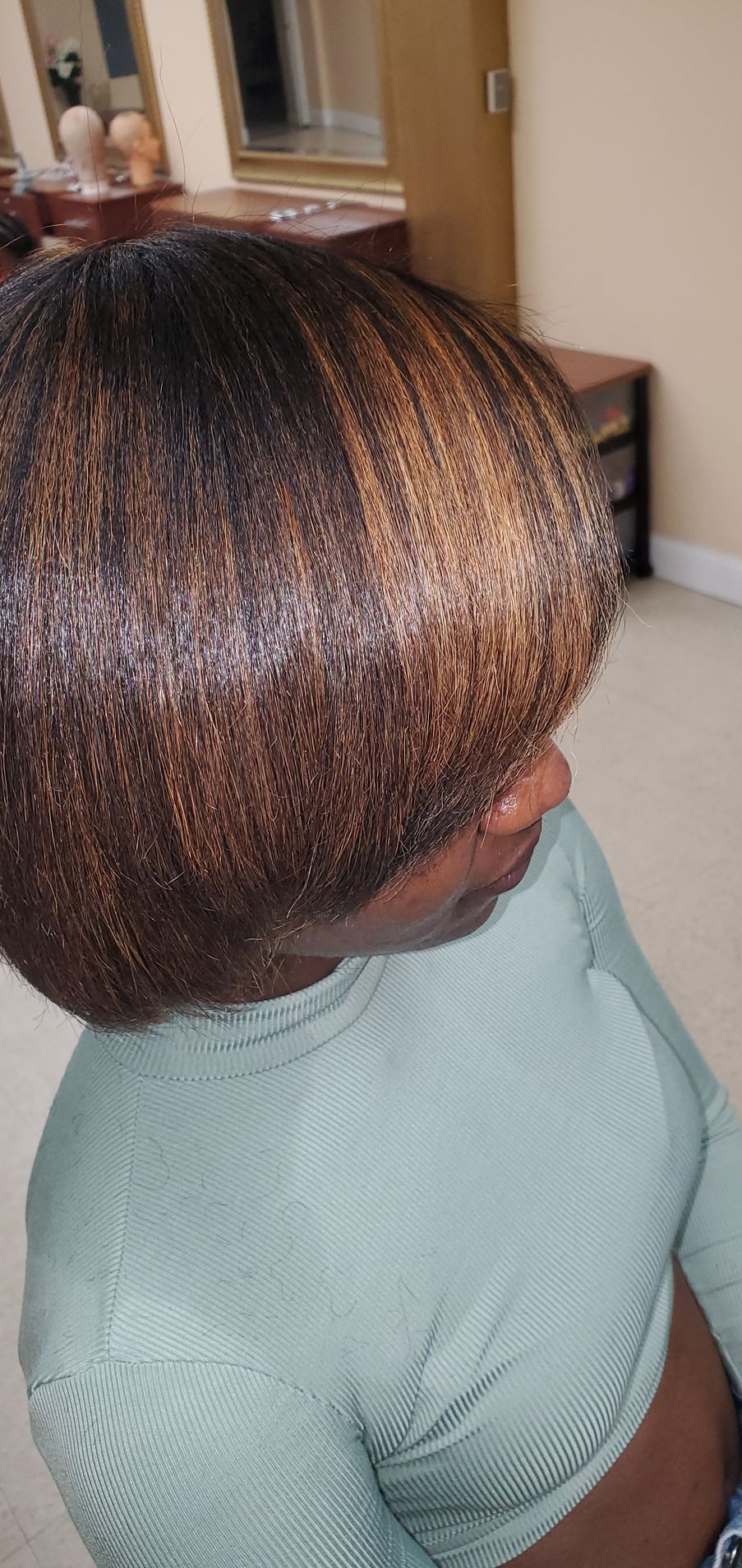 Side view of a person with short, highlighted hair wearing a light teal sweater indoors.
