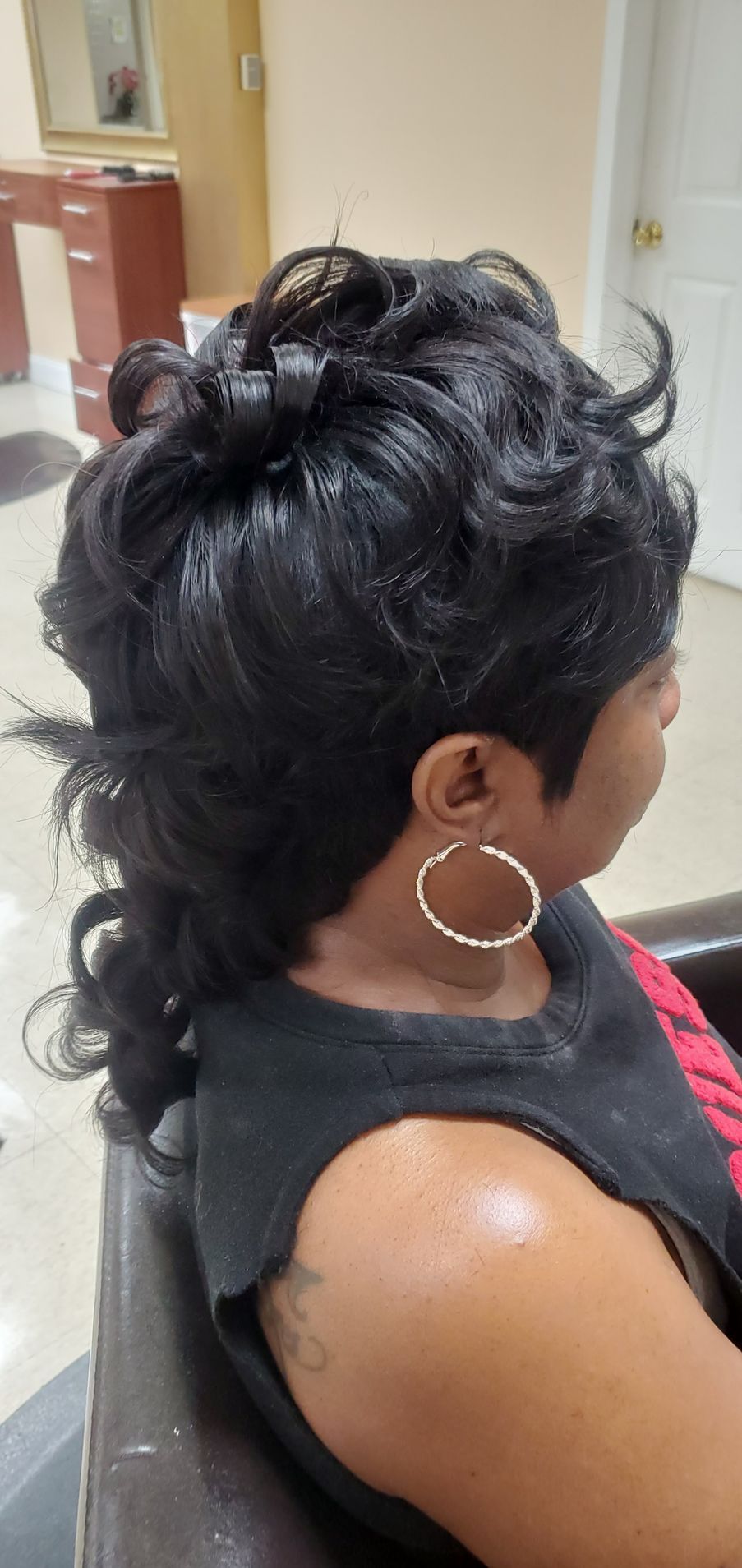 Side view of a woman with a curly updo hairstyle, wearing hoop earrings and a black top.