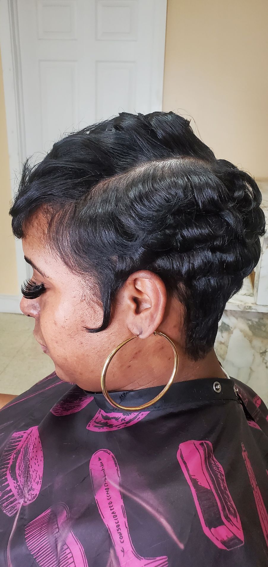 Side profile of a person with short braided hair and a large hoop earring, wearing a black and pink top.