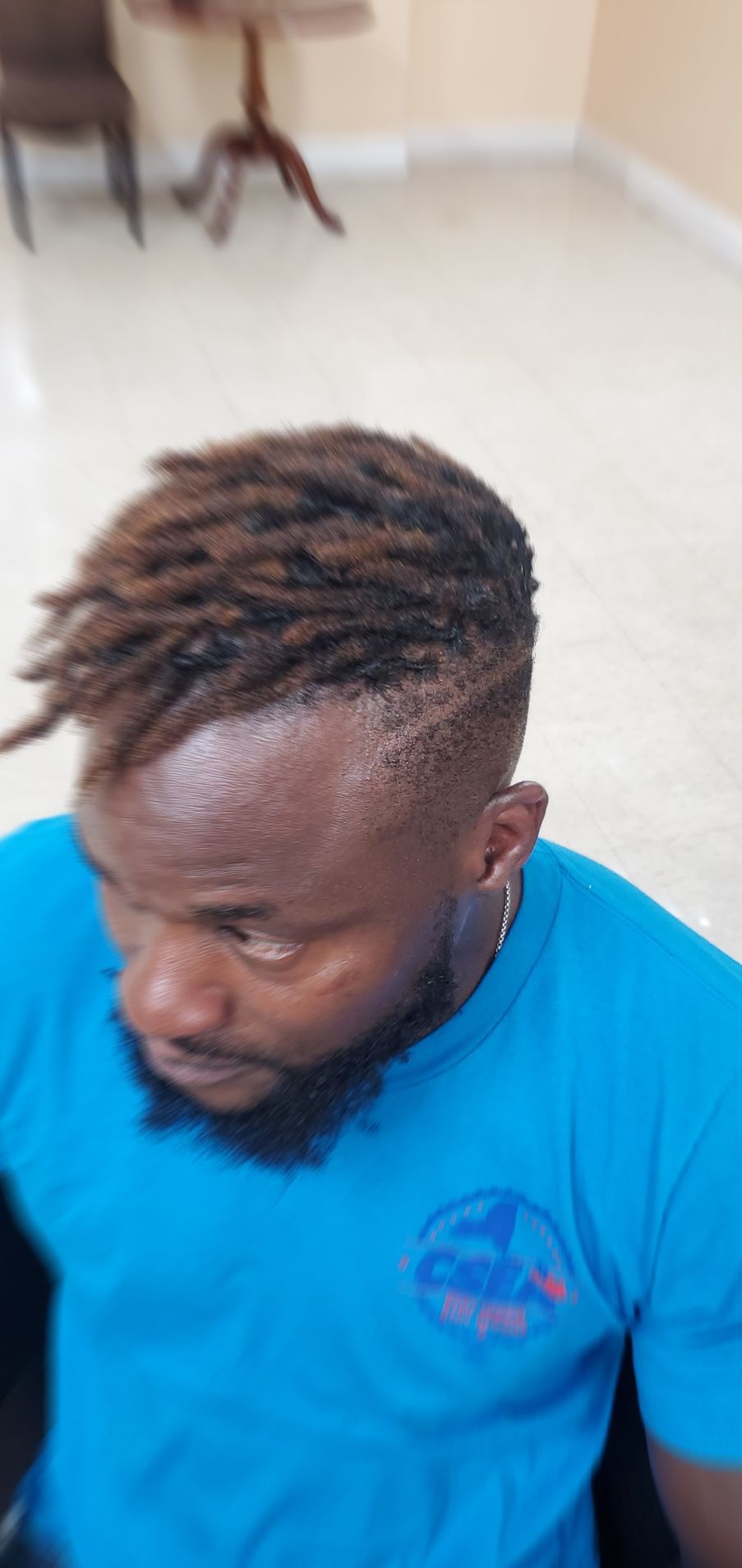 Man with short dreadlocks in a blue shirt looking down in a bright indoor room