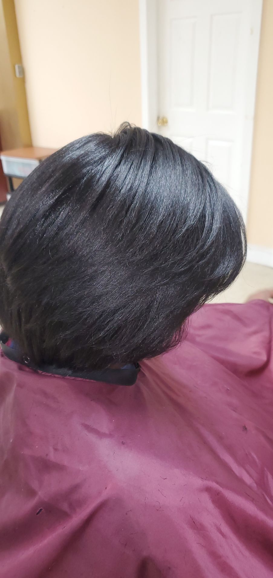 Close-up of a shiny black hairstyle on a maroon-covered chair.