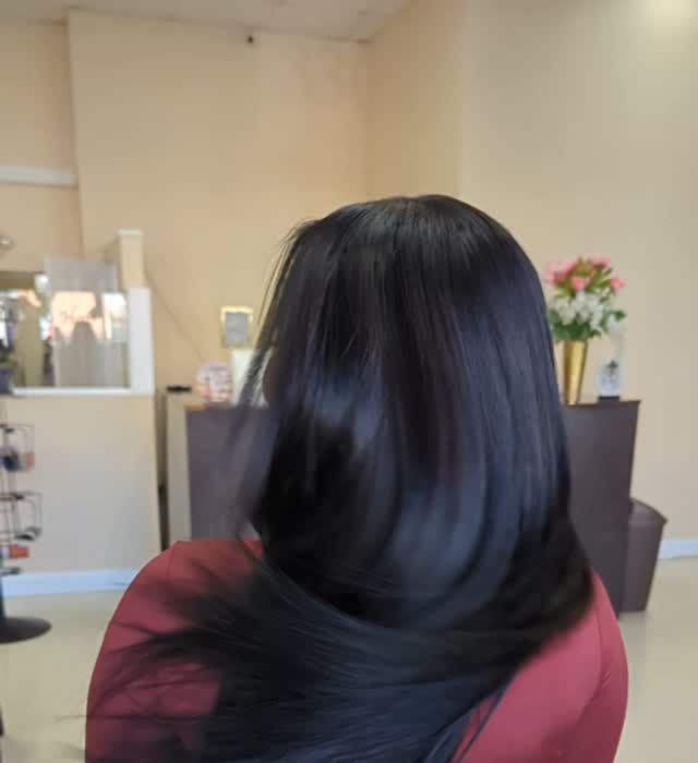 Person with long black hair in a maroon top, seen from behind in a salon or waiting area.