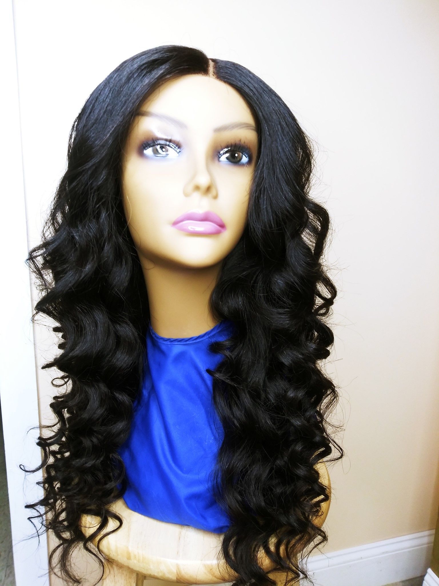 Mannequin head with long curly black hair, blue top, against a white wall