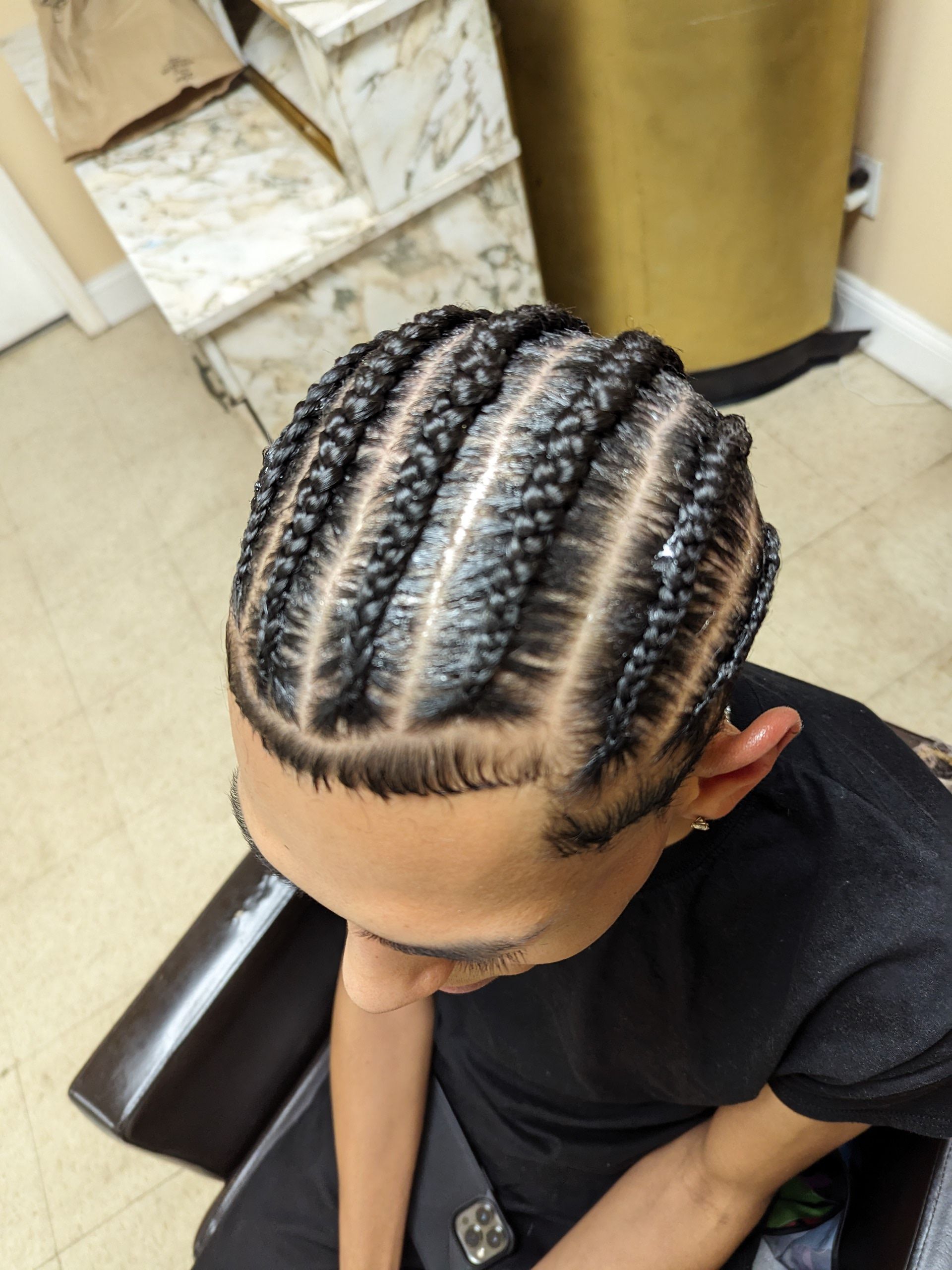 Child with neat cornrow braids seated in a salon chair, looking down.