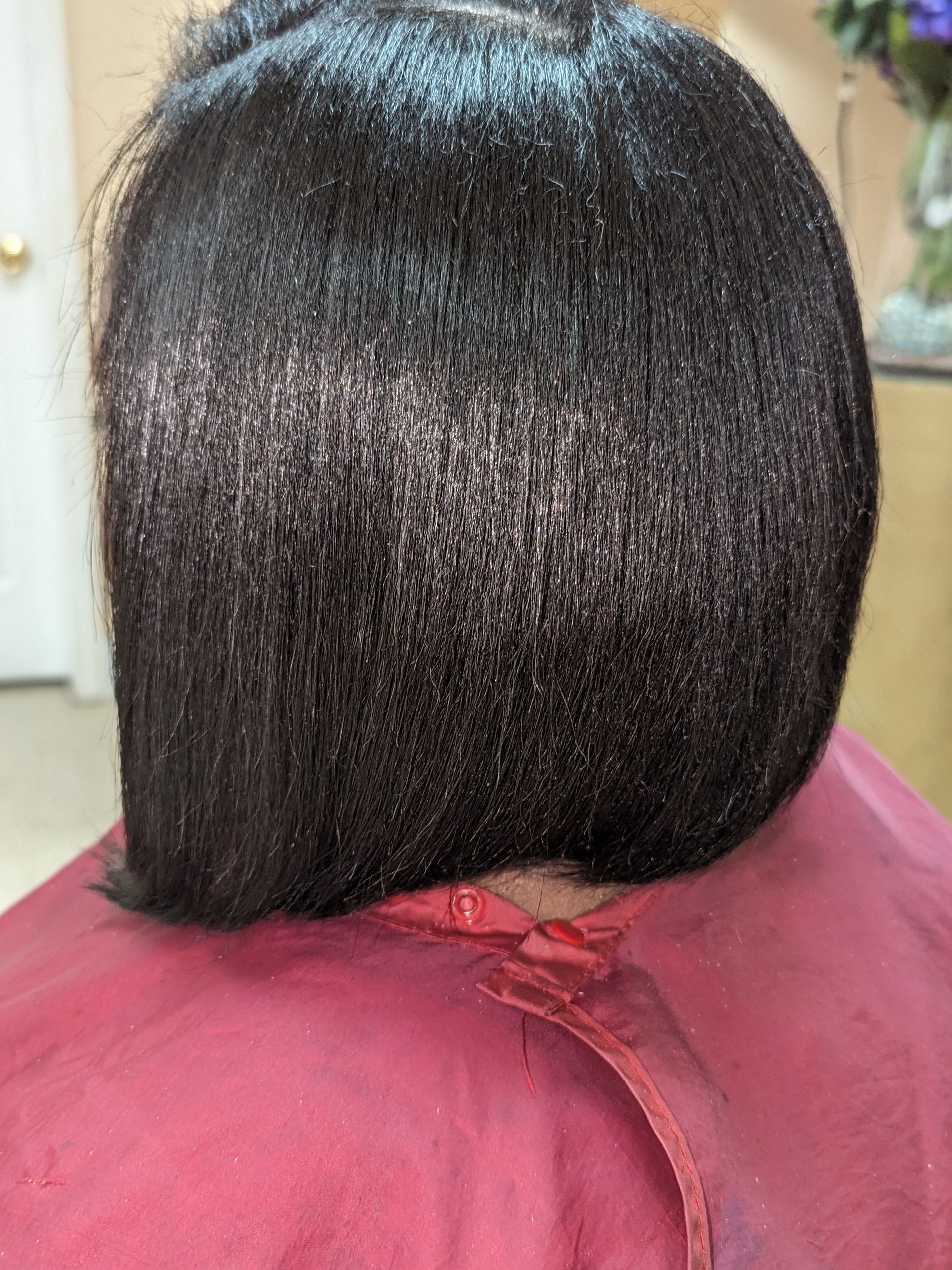 Back view of a sleek black bob haircut against a burgundy salon cape