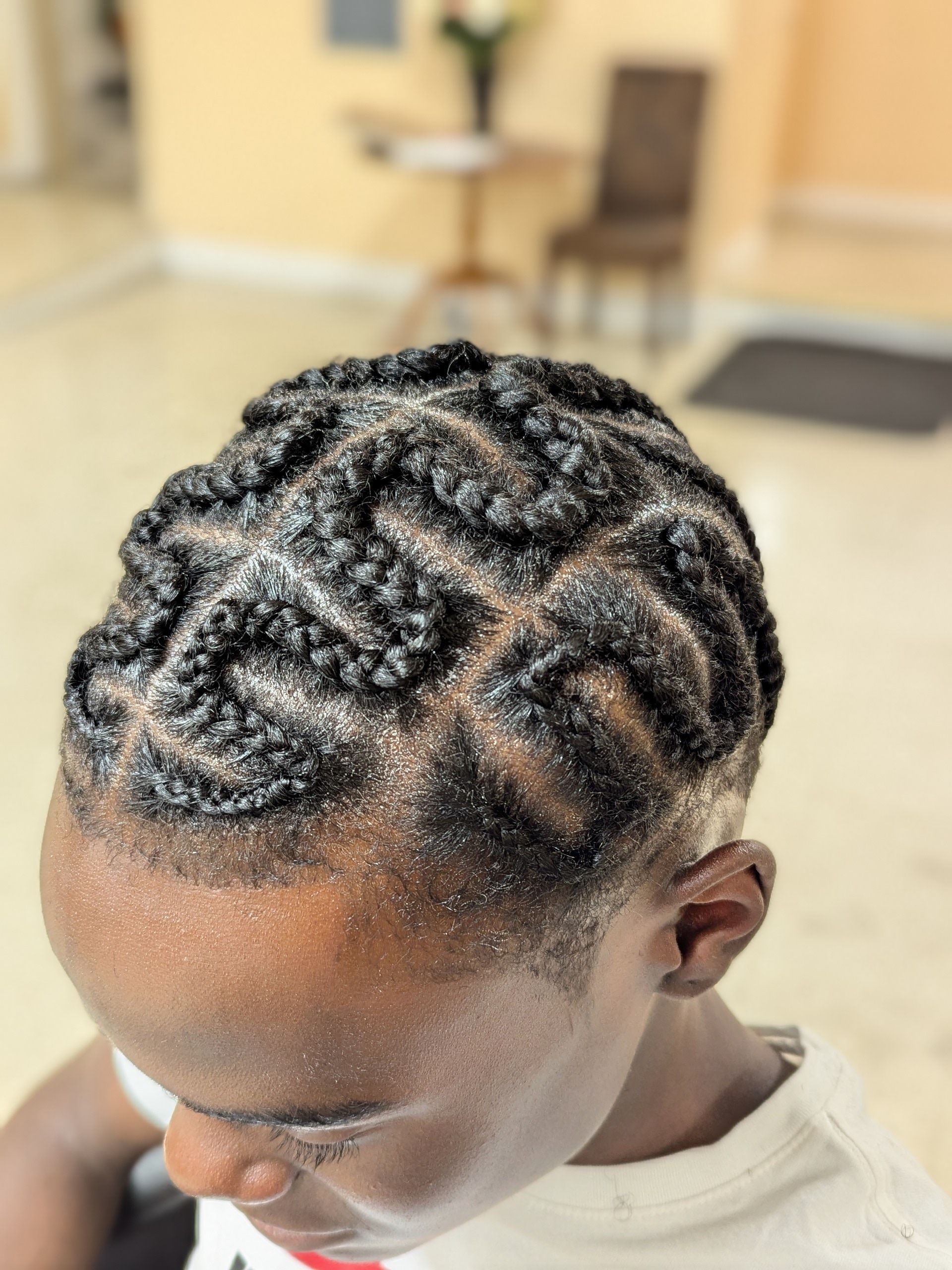 Close-up of braided hair with intricate zigzag cornrows, viewed from above in a bright indoor setting