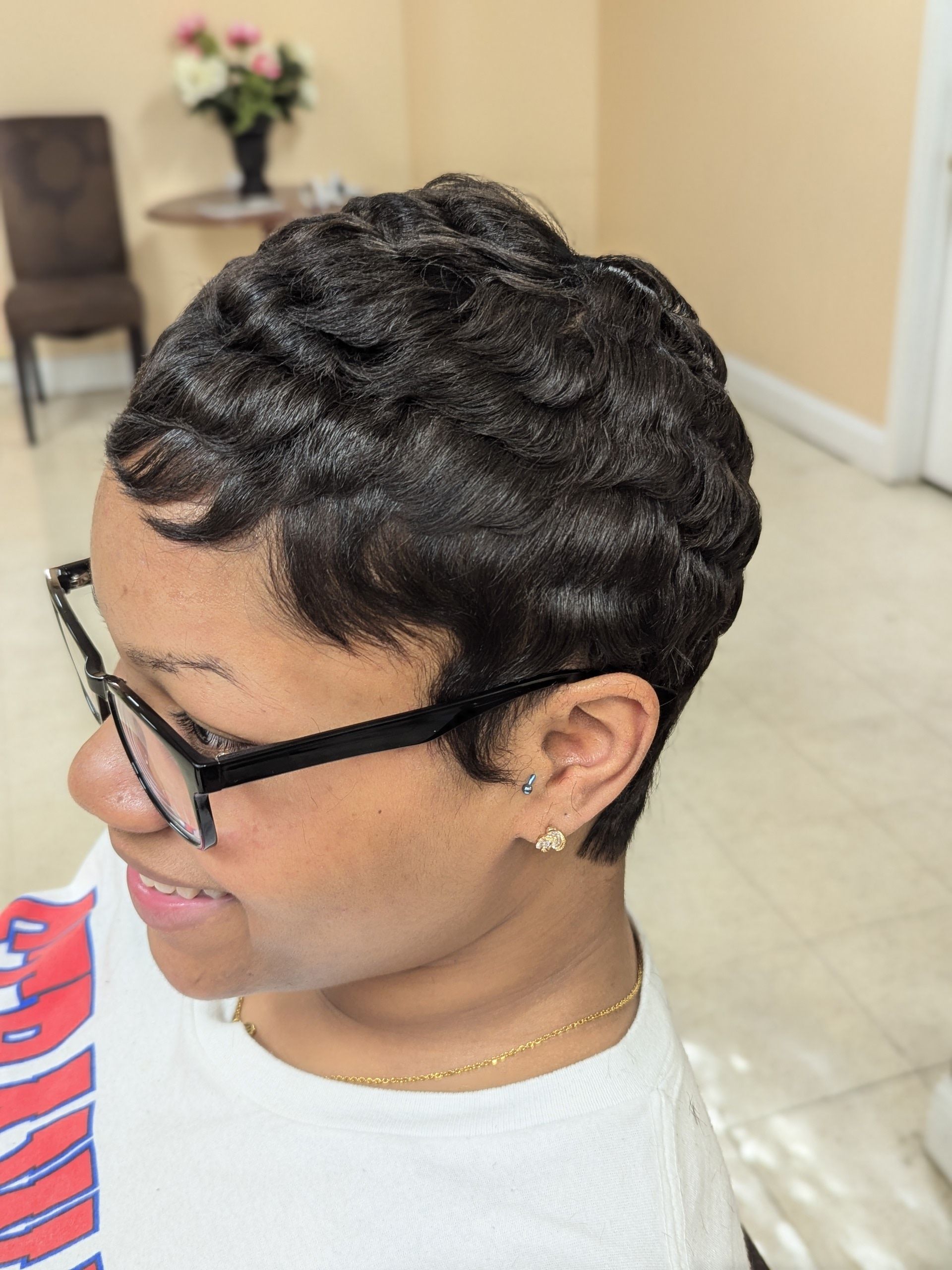 Short curly hairstyle in profile, wearing black glasses and a white shirt indoors.
