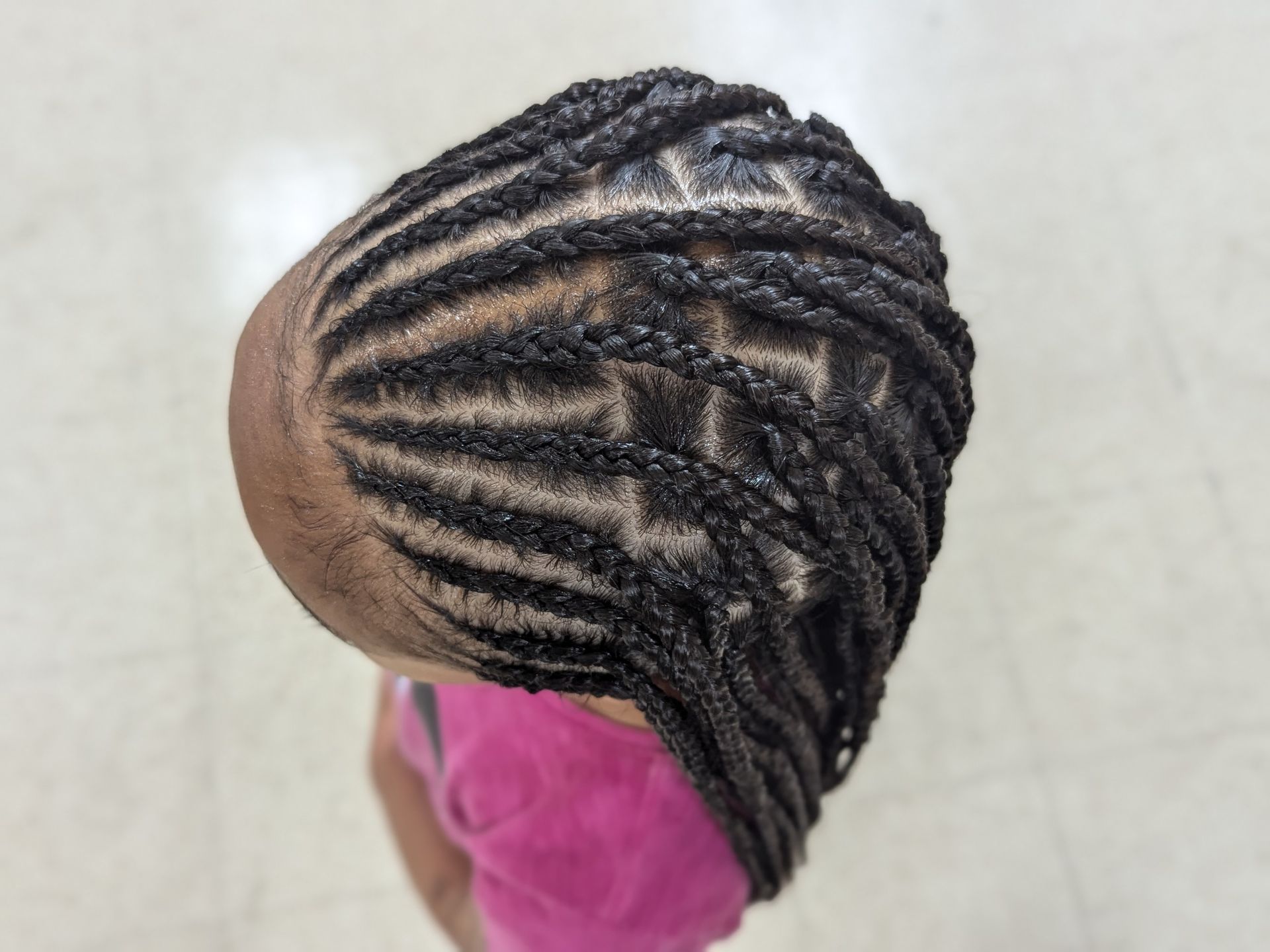Top view of a braided hairstyle with black cornrows and a pink shirt visible below