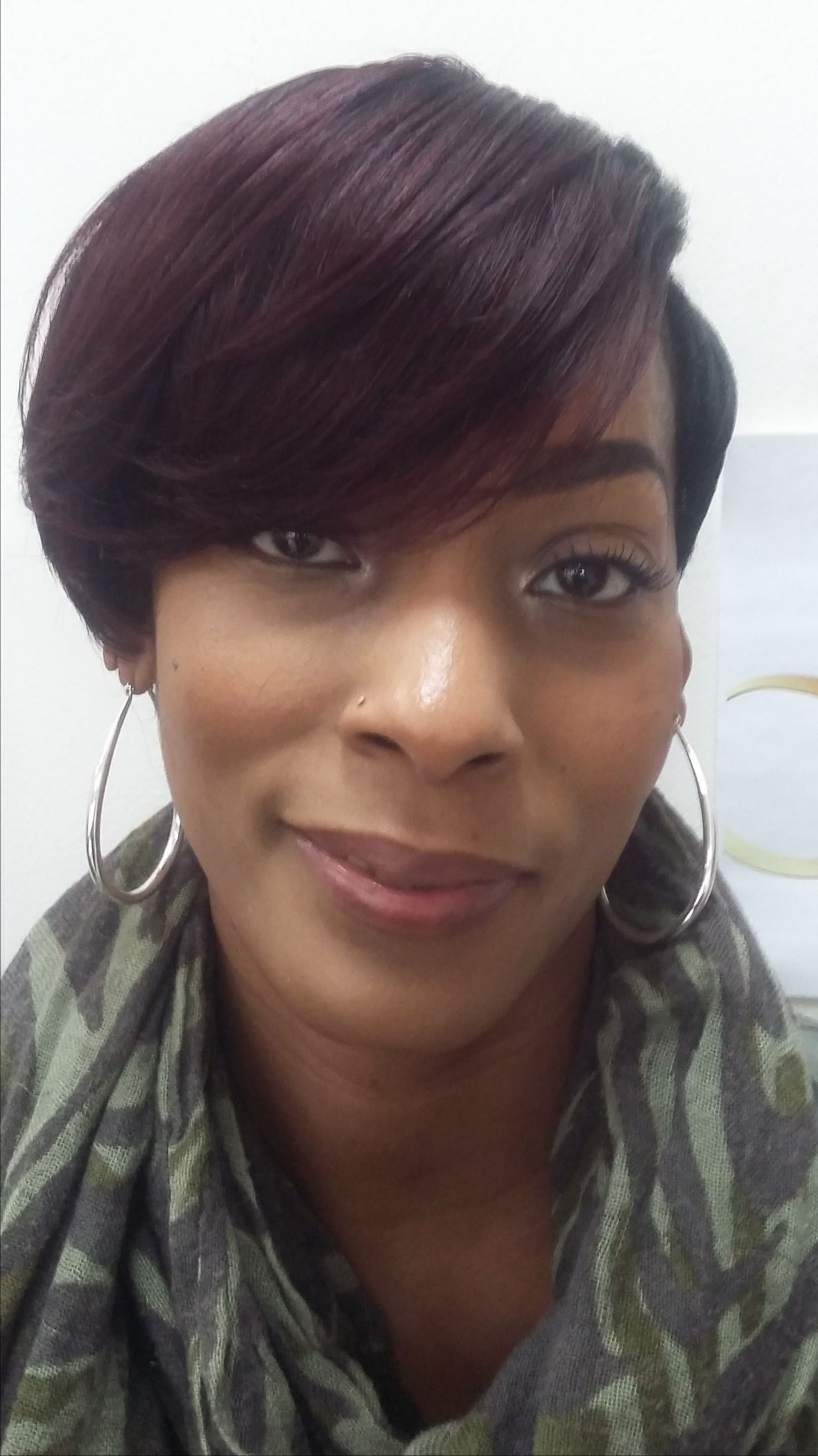 Close-up portrait of a person with short dark hair, hoop earrings, and a patterned scarf, smiling softly.