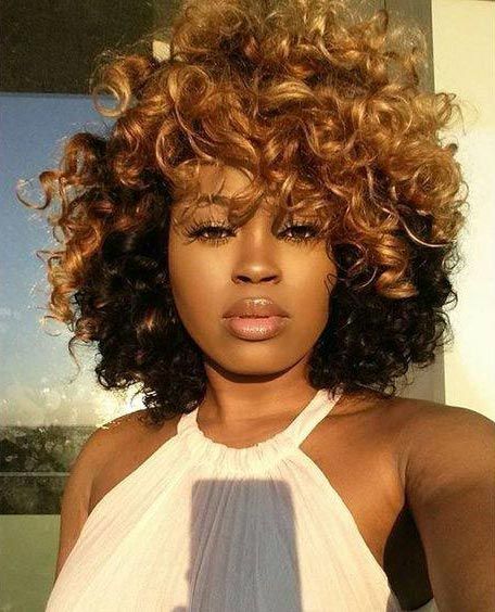 Portrait of a person with voluminous curly hair in a white halter top, standing in warm sunlight
