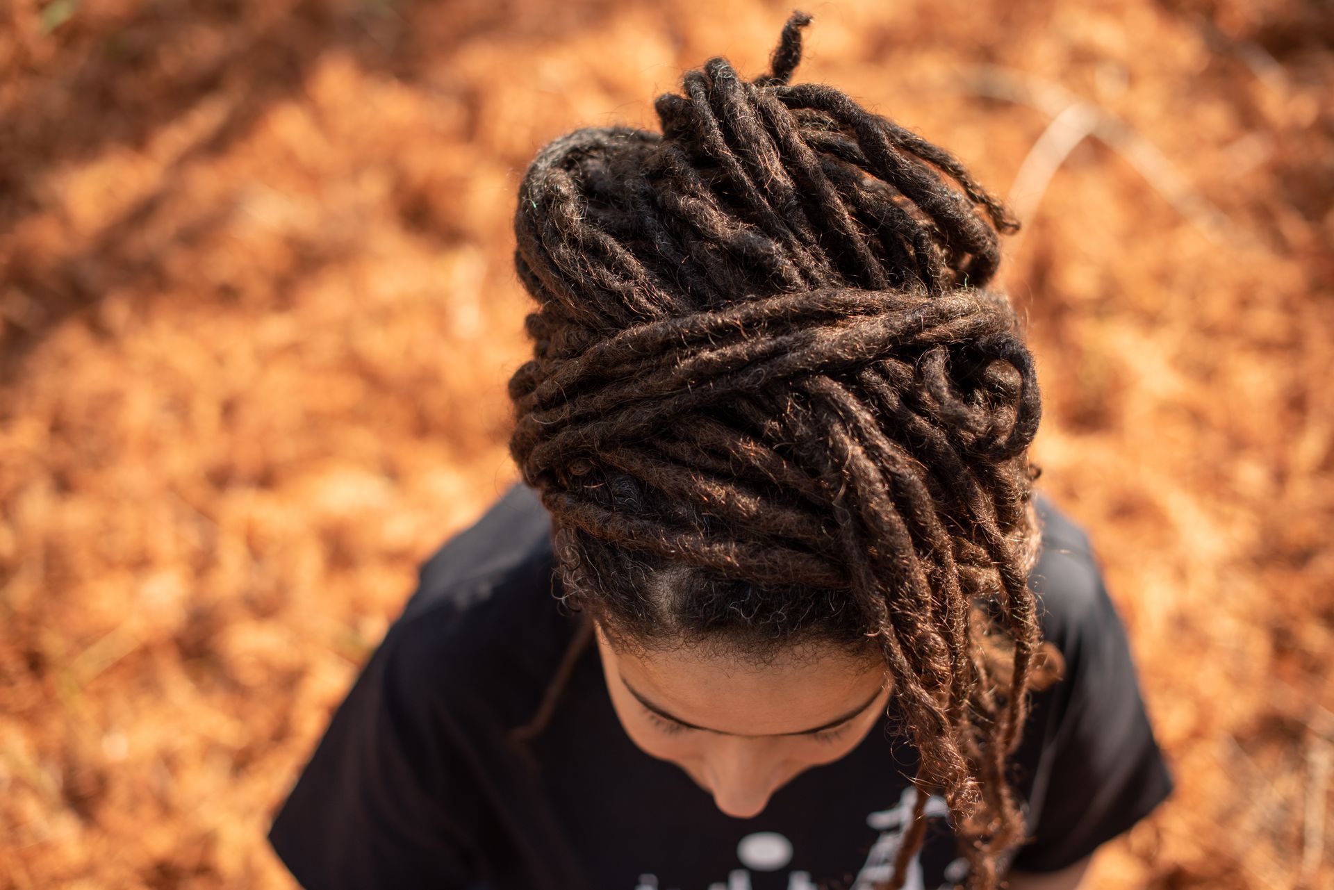 Top view of a person with long braided hair in a dark shirt against an orange leafy background