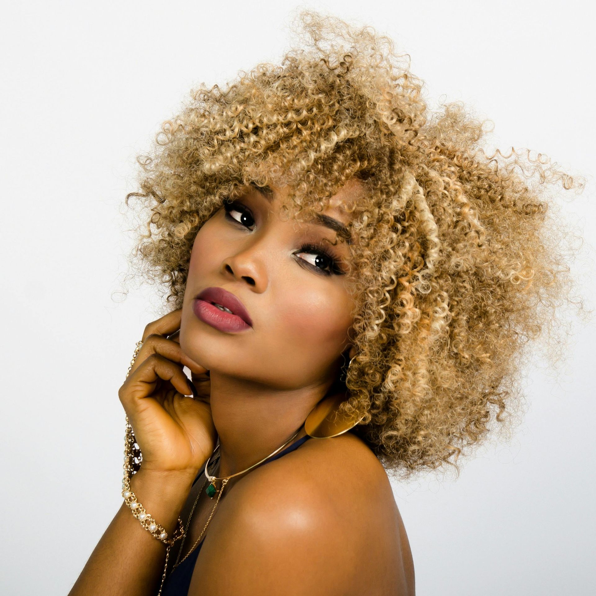 Portrait of a person with curly blonde hair, looking over a shoulder on a white background