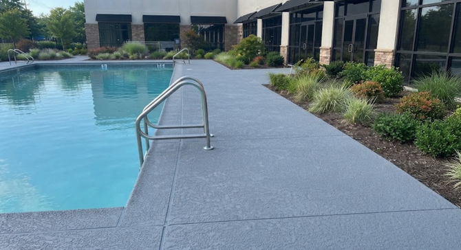 Outdoor pool deck with a metal handrail beside calm blue water and landscaped greenery