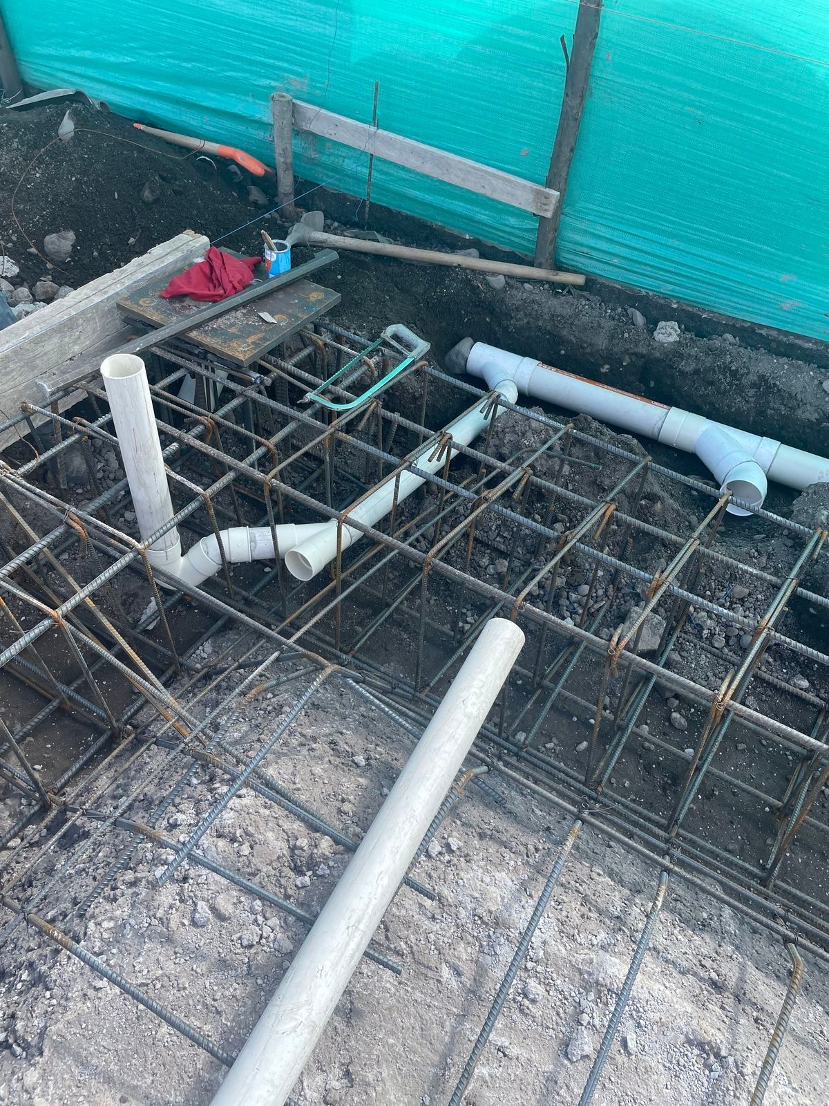 White PVC plumbing pipes installed within a steel rebar foundation cage on a construction site.