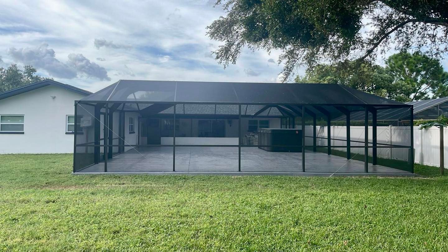 Screened patio with dark frame and roof, concrete floor, hot tub, and house in the background.