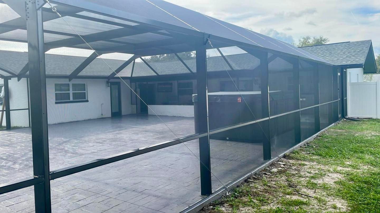 Screened-in patio attached to a house with black frames, rain gutters, and a grassy lawn.