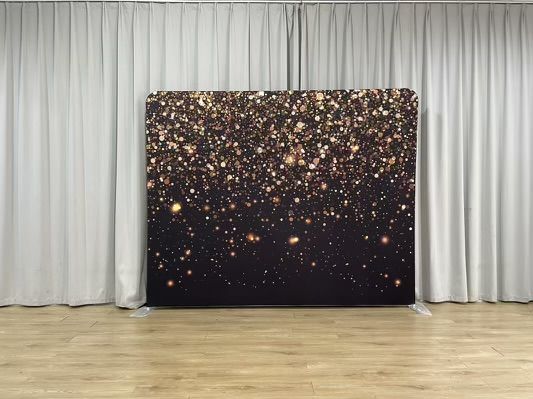 A black and gold backdrop is sitting in front of a white curtain in a room.