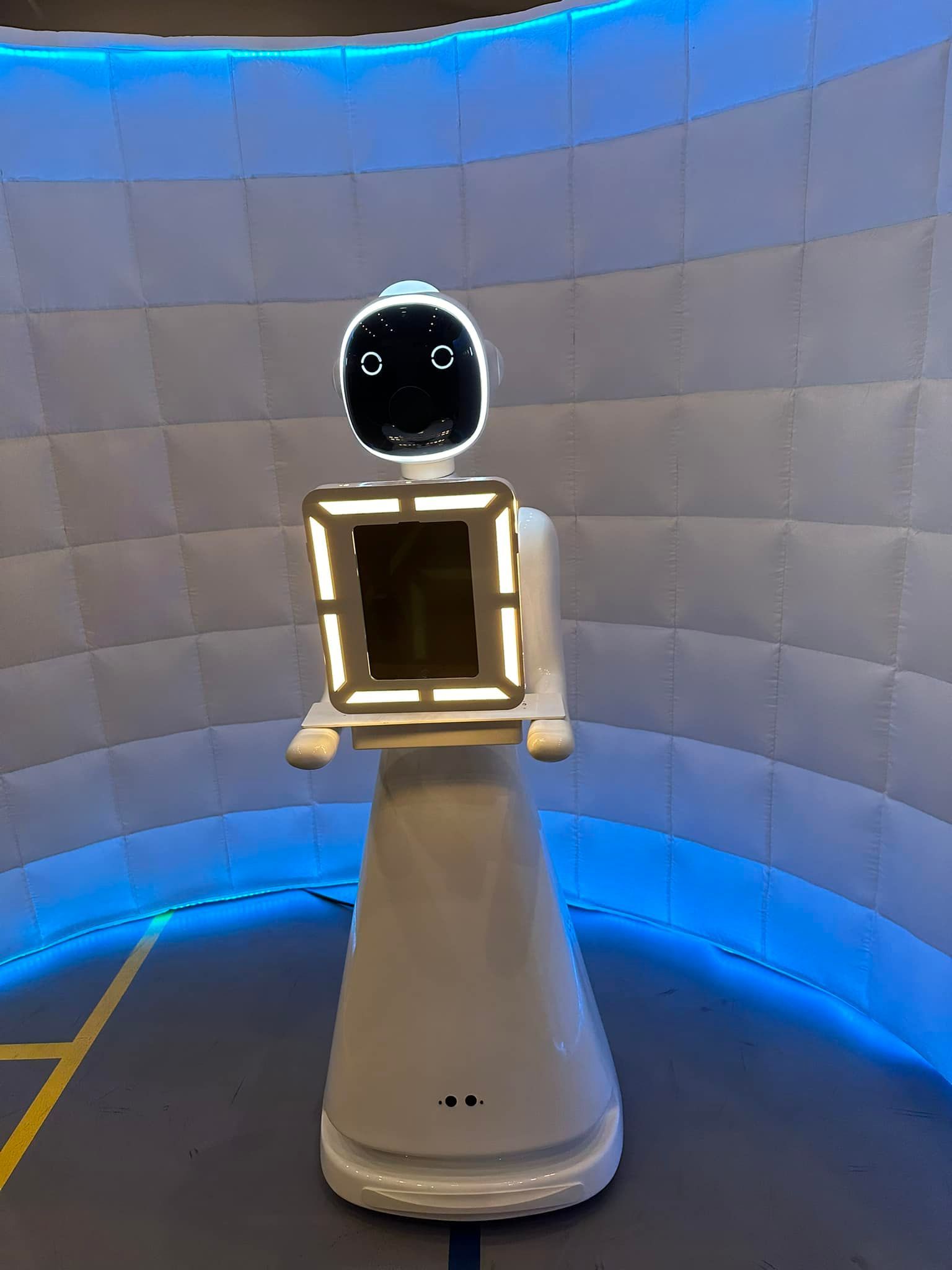 A white robot is standing in front of a blue wall.
