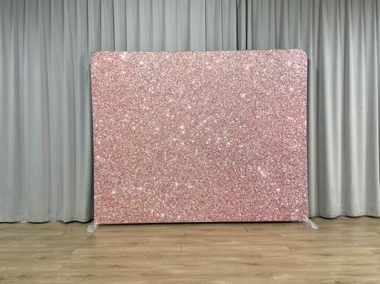 A pink glitter backdrop is sitting in front of a white curtain in a room.
