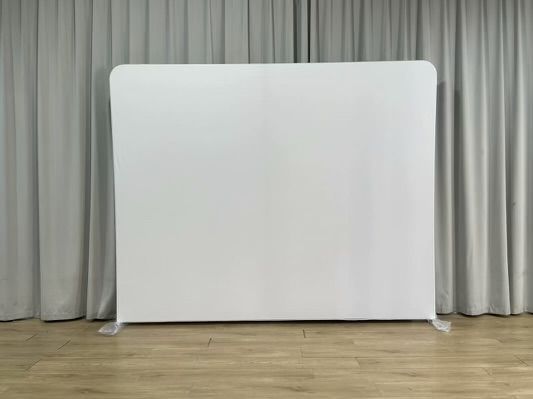 A white backdrop is sitting on a wooden floor in front of a white curtain.