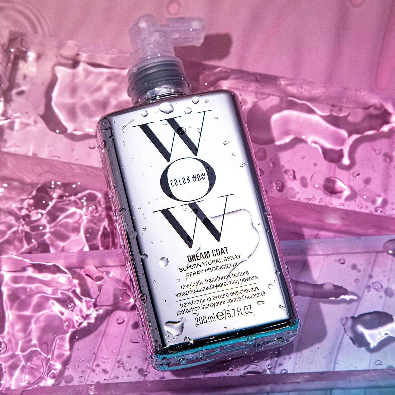 Silver WOW shampoo bottle with water droplets, resting on a pink and blue surface.