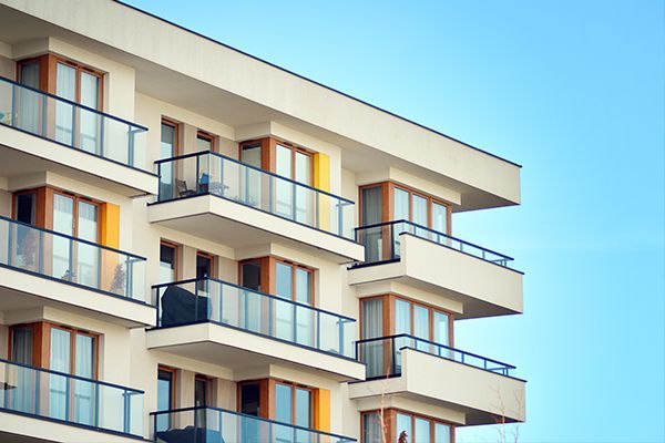 A modern, light-colored multi-story apartment building with balconies and glass railings against a blue sky.