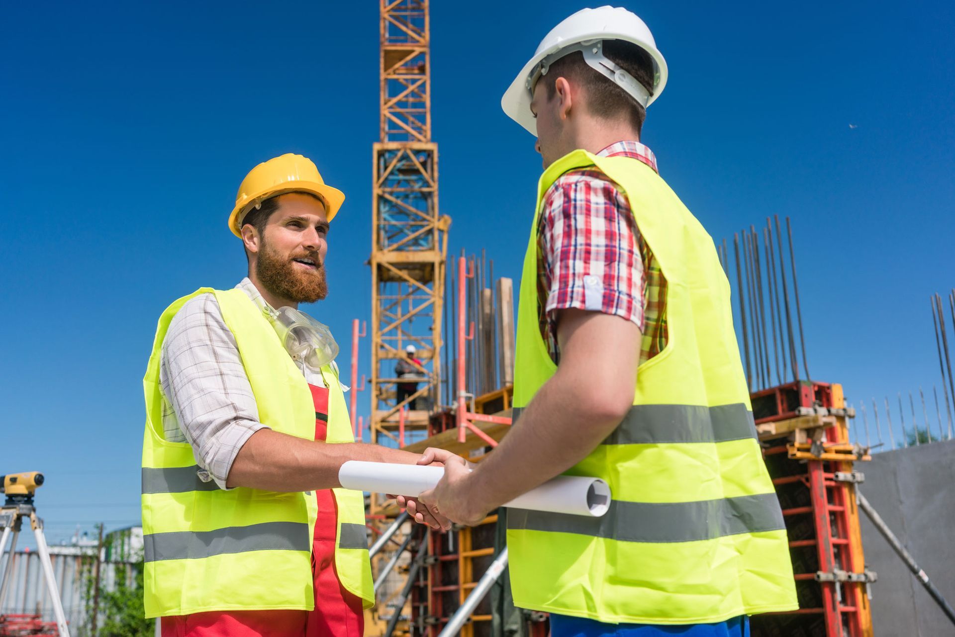 Two construction workers shaking hands on a construction site, a blue sky background.