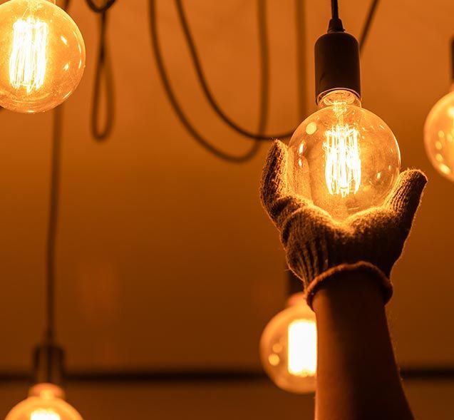 Gloved hands holding a glowing light bulb among several warm hanging bulbs Gloved hands holding a glowing light bulb among several warm hanging bulbs