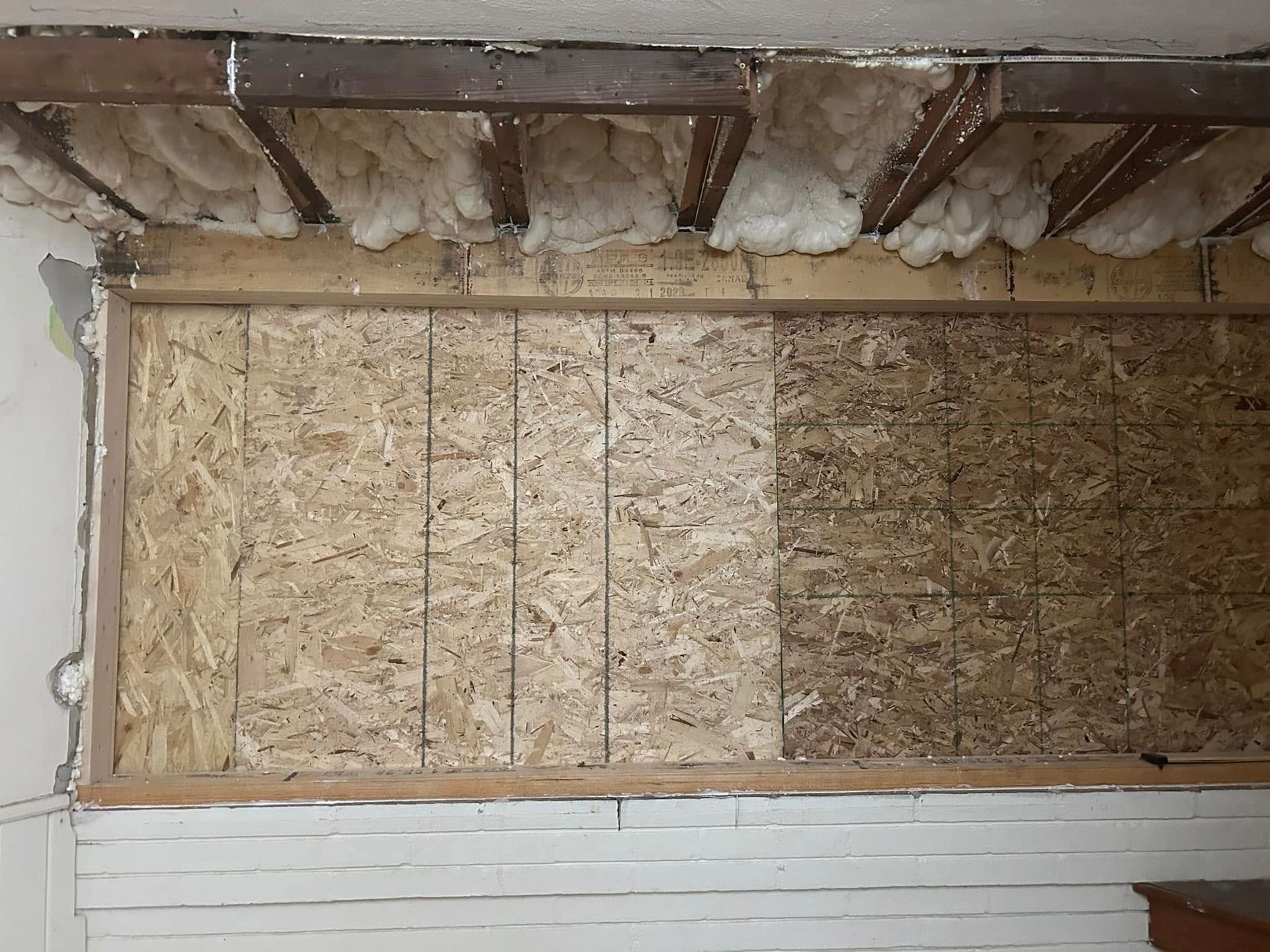 Exposed wall with OSB paneling, wooden frame, insulation, and white trim.
