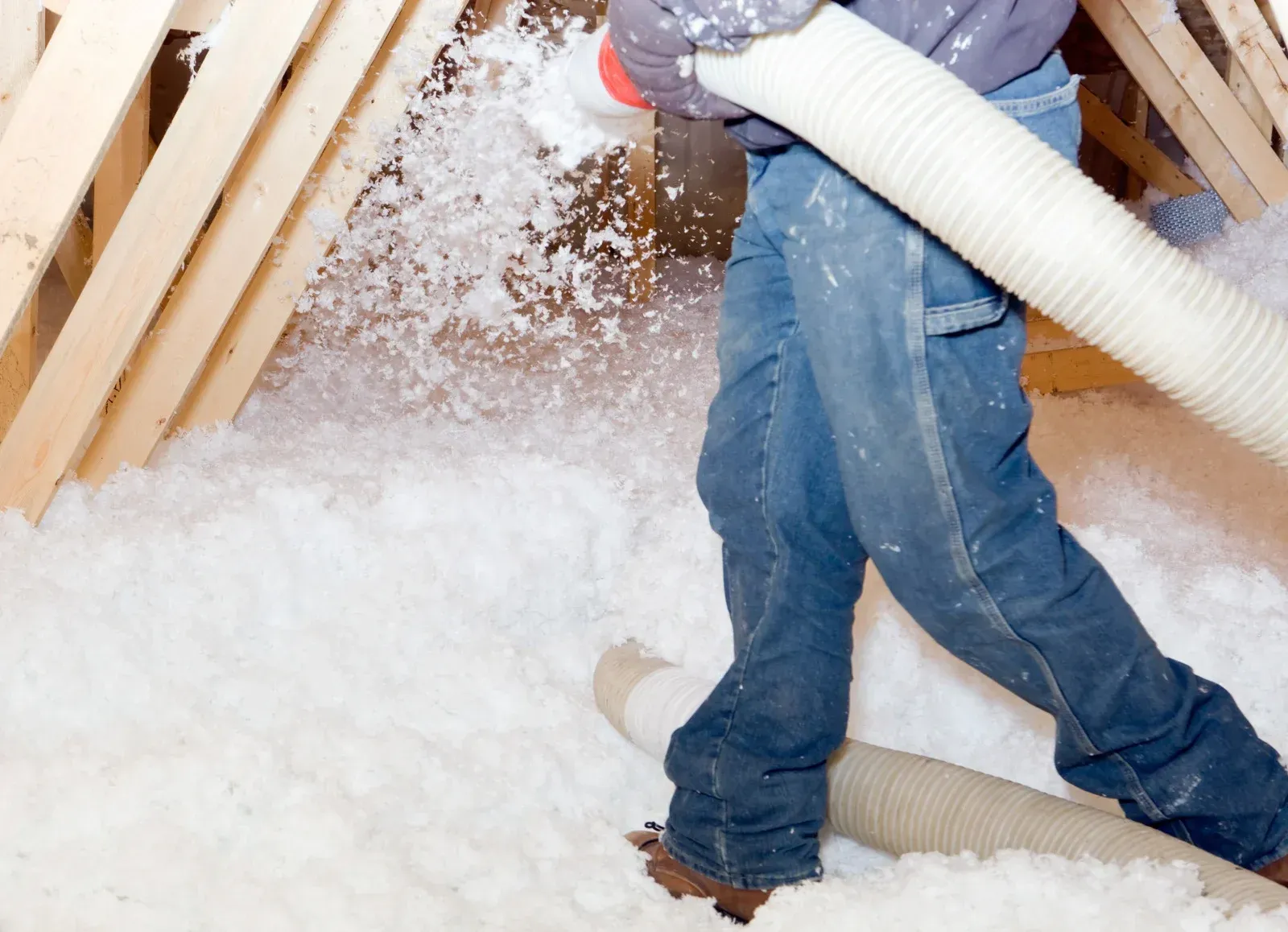 Person blowing insulation into an attic from a hose. White insulation fills the space.