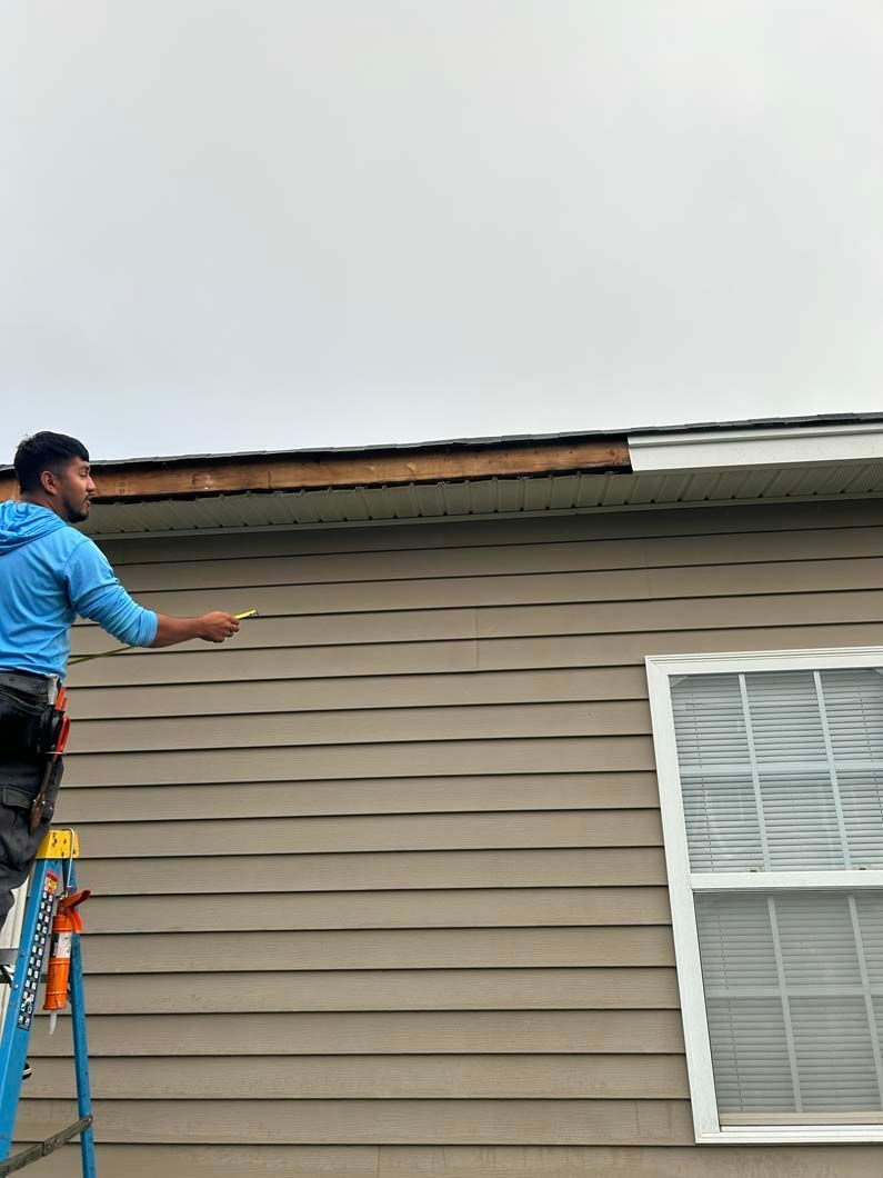 A man is standing on a ladder painting the side of a house.