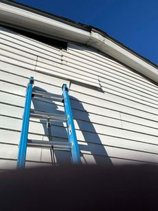A blue ladder is leaning against a white house