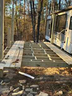 A wooden deck is being built next to a rv in the woods.