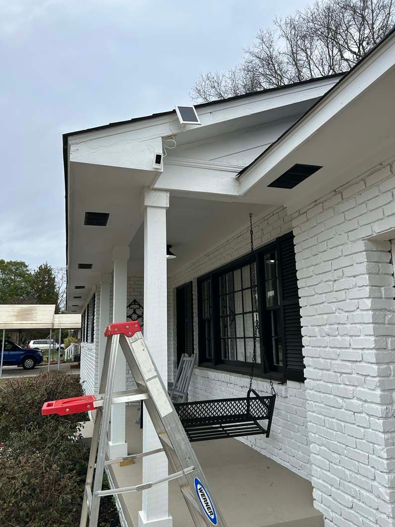 A ladder is sitting on the porch of a white brick house.