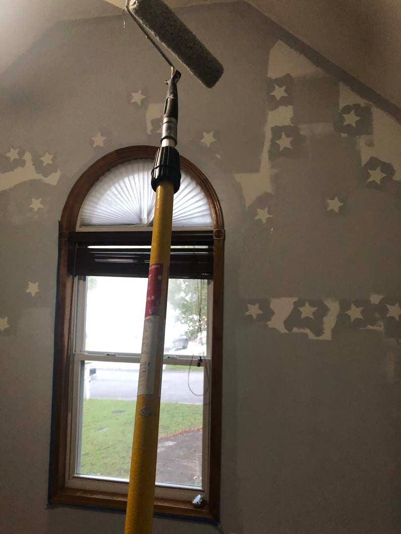 A paint roller is hanging from a pole in front of a window.