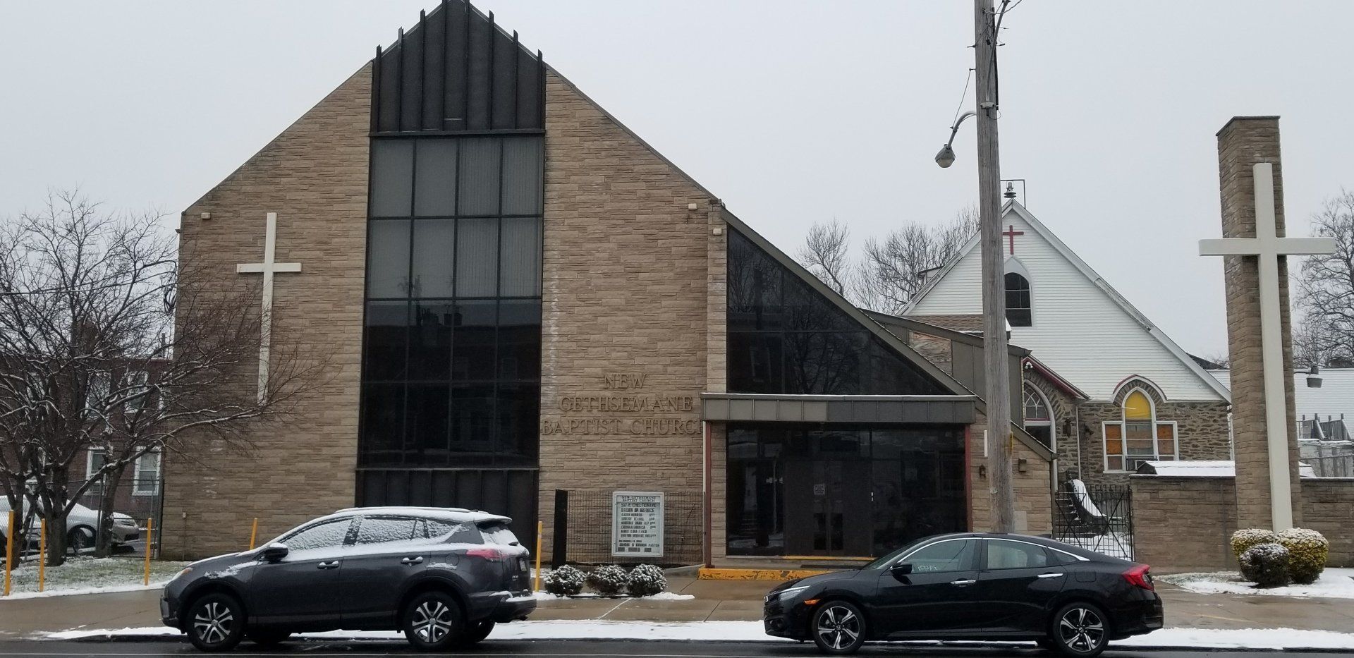 Brick church with a tall glass entrance and cross, seen on a snowy street with parked cars