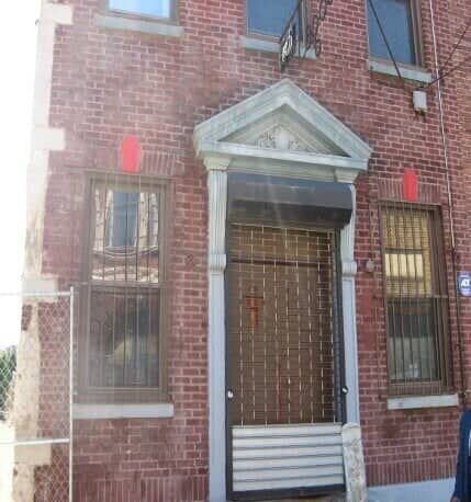 Brick townhouse entrance with barred door, white trim, and two windows on either side