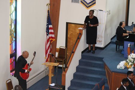 Church sanctuary with a guitarist playing beside the pulpit and a woman standing at the lectern on the steps